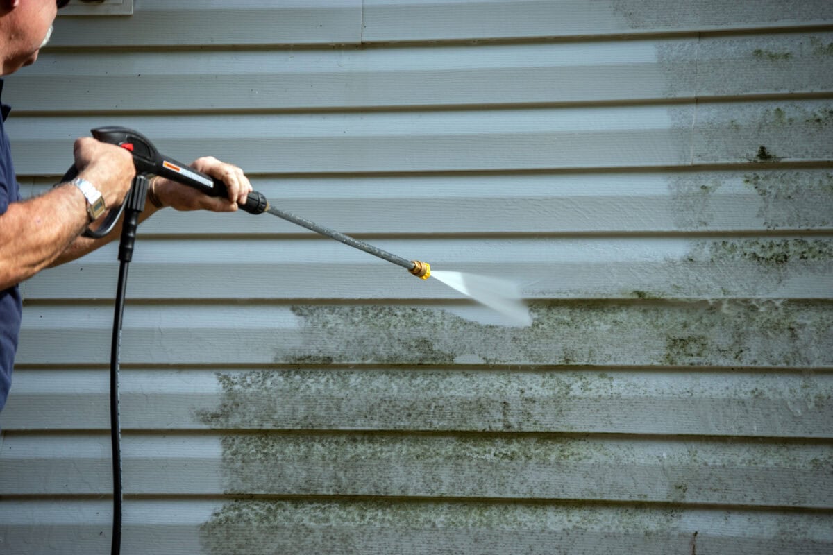 Man uses power washer to clean siding