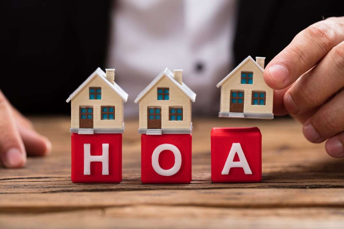 Businessperson's hand placing house model over red HOA blocks on wooden desk